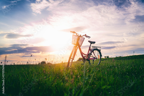 Female bicycle with a basket stands on a green field at sunset, summer vacation adventure