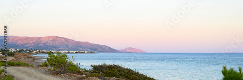 seascape at dusk. a dirt road, a city in the distance and mountains with a gentle pink sunset and a beautiful blue sea. banner