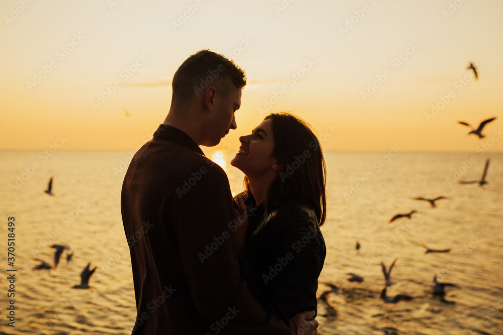 Loving couple outdoor at sunset.  Profiles of romantic couple looking at each other on background of sea sunset and flying seagulls. Copy space.
