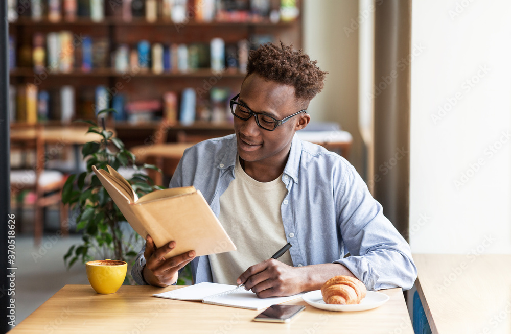 Cool black guy reading book and taking notes during his studies at cafe Cool black guy reading book and taking notes during his studies at cafe