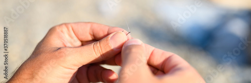 men s hands tying a fishing line on a fishing hook. selective focus. step 2. banner