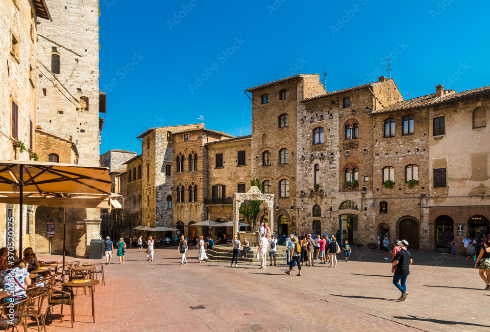 Lovely view of the popular Piazza della Cisterna, the main square of San Gimignano, Tuscany, Italy. Surrounded by medieval houses, the cistern is capped by a travertine octagonal pedestal.