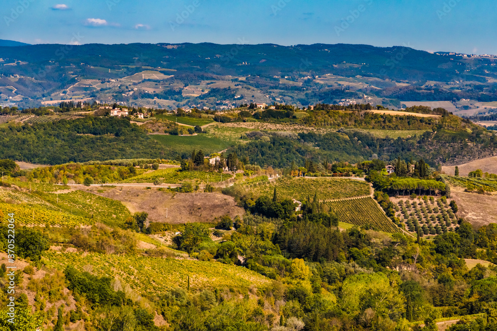 Stunning view across the agricultural valleys in the countryside of the medieval hill town San Gimignano. A typical landscape with houses, olive tree orchards and vineyards on a sunny day in Tuscany.