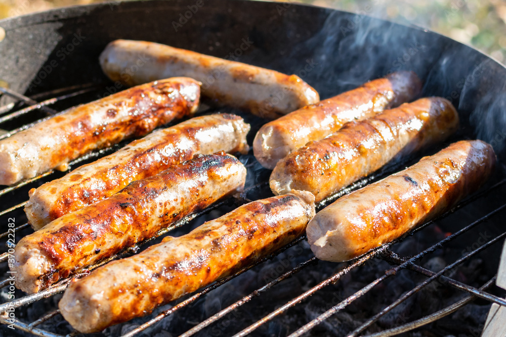 BBQ sausages are cooked on the grill in the meadow in the park on a sunny autumn day, closeup. Delicious juicy hot meat meal with smoky, backyard weekend barbeque picnic, family holiday meal.
