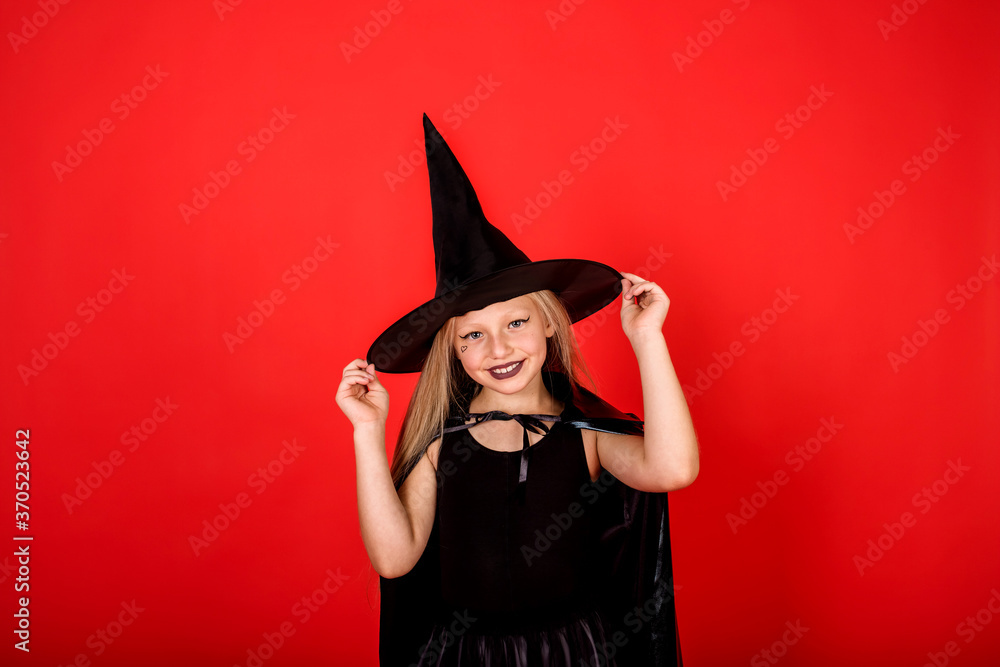 laughing girl in a witch costume holding hands hat on a red background with a copy of space laughing girl in a witch costume holding hands hat on a red background with a copy of space