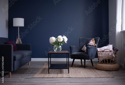 Fototapeta Naklejka Na Ścianę i Meble -  Bright interior of the living room. Blue wall, gray chair and coffee table. Natural decor woven basket. White peonies in a glass vase