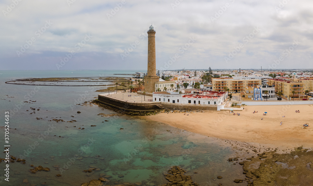Fototapeta premium An aerial view with the drone of the big lighthouse of Chipiona on the Atlantic Ocean in western Spain. It's a cloudy summer day. In the foreground is a beach.