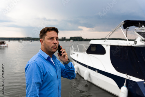 Man talking on the phone beside luxury yacht at port. Nautical and marine concept