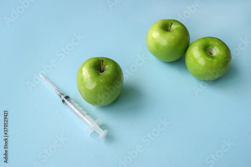 Green apple and syringe with GMO on a blue background.