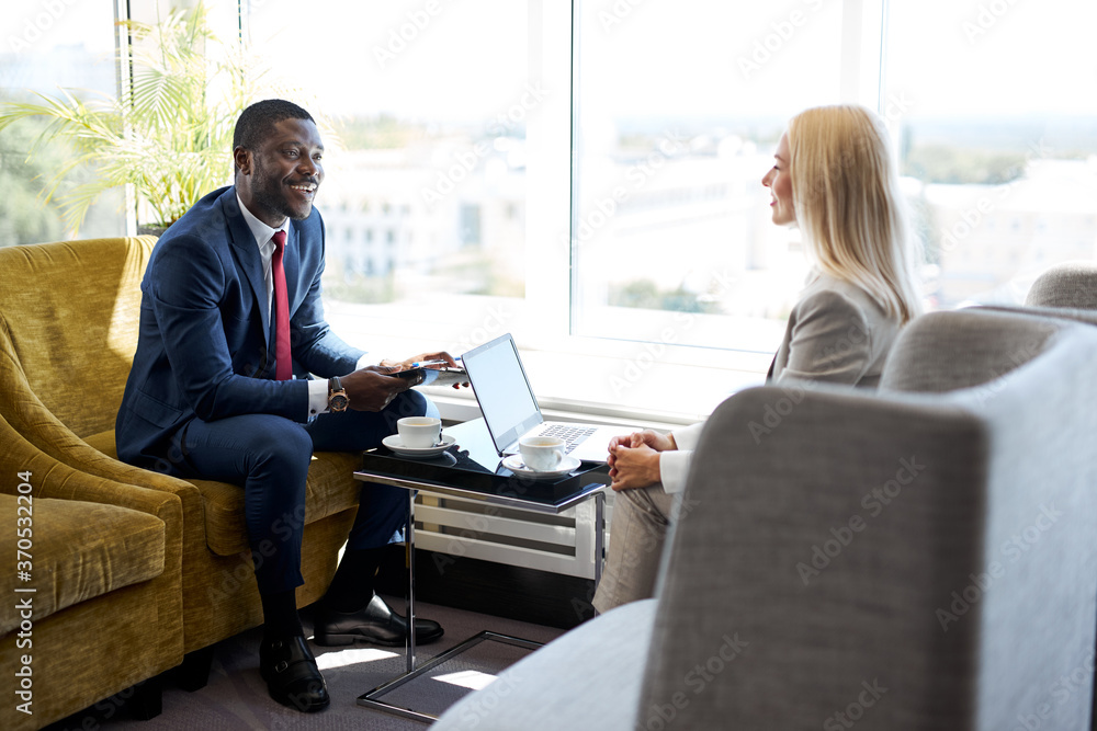 business partners have conversation in lobby of hotel, african and caucasian people talk, discuss, use laptop, in elegant clothes business partners have conversation in lobby of hotel, african and caucasian people talk, discuss, use laptop, in elegant clothes