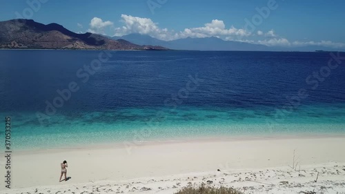 A woman in bikini standing at the shore of an idyllic beach in the nearby of Maumere, Indonesia. The islands are surrounded by crystal clear water and flourishing coral reef. Snorkelling spot. Beauty
 photo