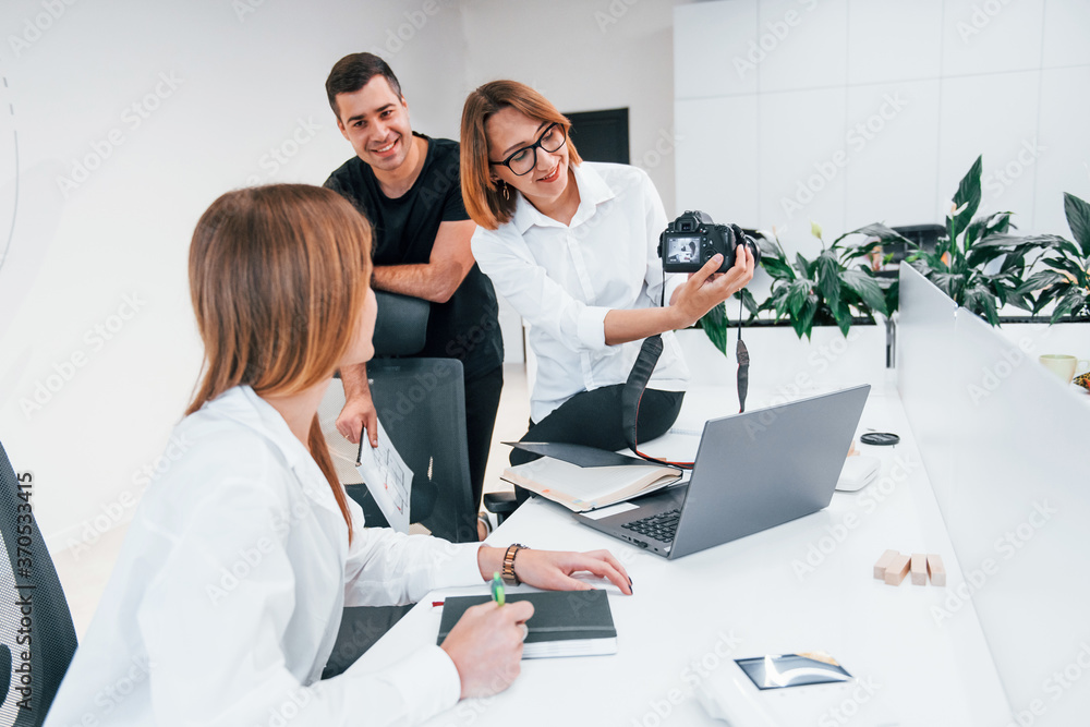 Group of business people in formal clothes indoors in the office looking at photos on the camera Group of business people in formal clothes indoors in the office looking at photos on the camera
