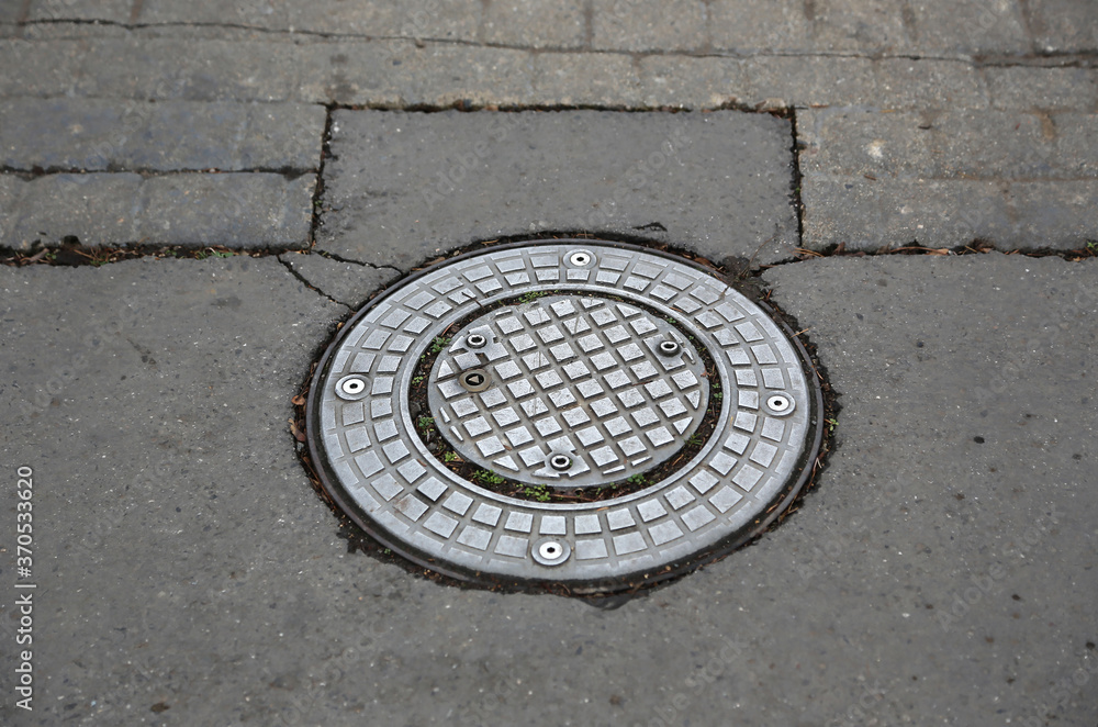 Metal manhole cover on rough cobblestone and asphalt street