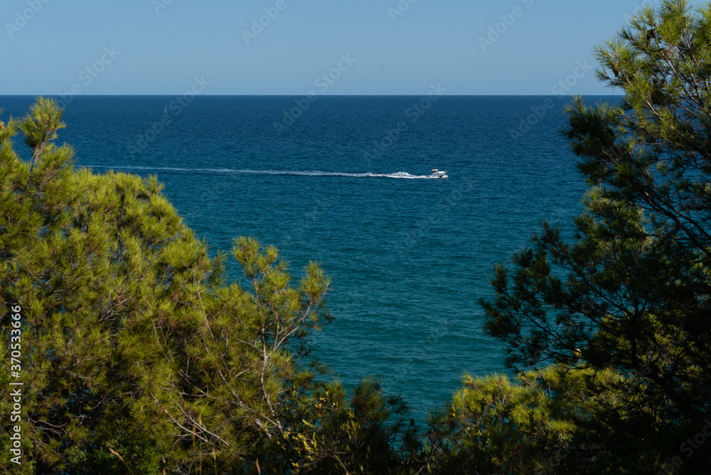 View of the beautiful blue Mediterranean sea with rocks near the shore with waves on a sunny day with boats and sailboats