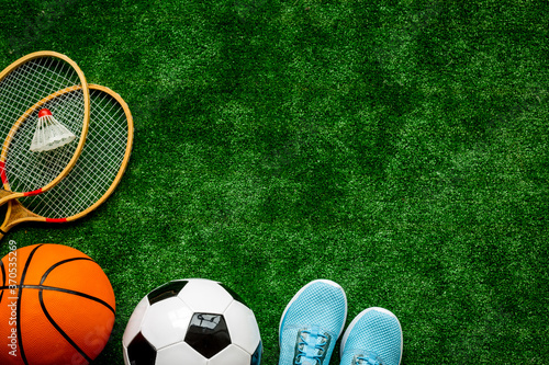 Sport balls and badminton rackets on football grass. Top view copy space