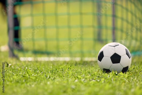 Soccer ball on the grass of football field. Soccer goal and goalkeeper in a blurred background.