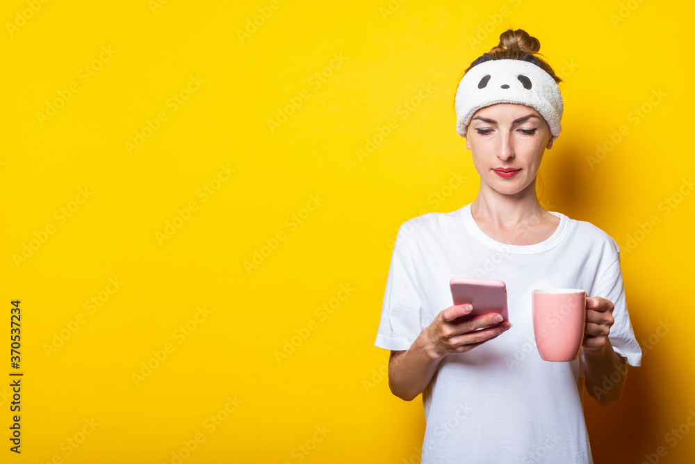 Beautiful young woman with a phone and a cup of coffee on a yellow background Beautiful young woman with a phone and a cup of coffee on a yellow background