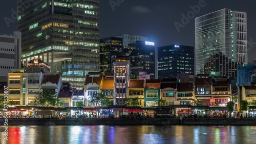 Singapore quay with mall restaurants and tall skyscrapers in the central business district on Boat Quay night timelapse hyperlapse. Houses reflected in water photo