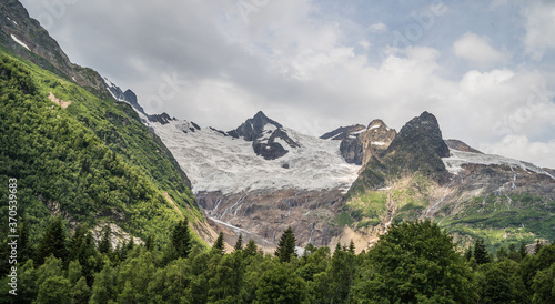 Beautiful landscape of glacier in summer season. Glacier mountain with green vegetation on high ground in cloudy weather.