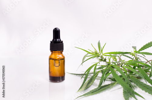 Bottle with cannabis oil against hemp leaves on a white background.