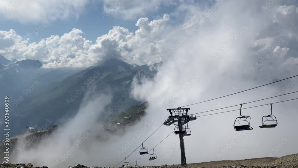 Clouds enveloping modern ropeway with benches in amazing mountainous terrain. Clouds enveloping modern ropeway with benches in amazing mountainous terrain.