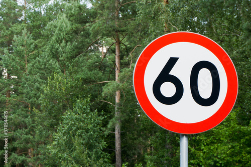 Speed limit sign with trees behind. Maximum sixty kilometers per hour. Safety on road in forest background. White round sign red border line.