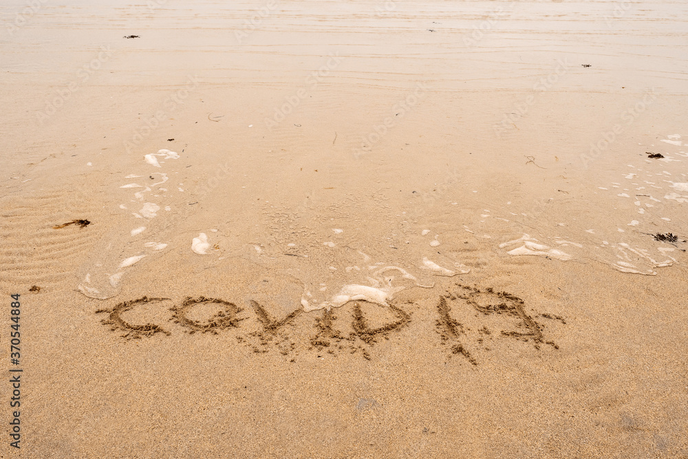 Sign on a yellow sand COVID 19 being washed away by a wave. Sign on a yellow sand COVID 19 being washed away by a wave.