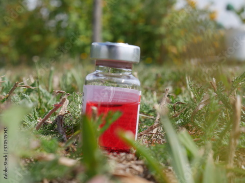 red bottle with medicine and a syringe on the background of grass