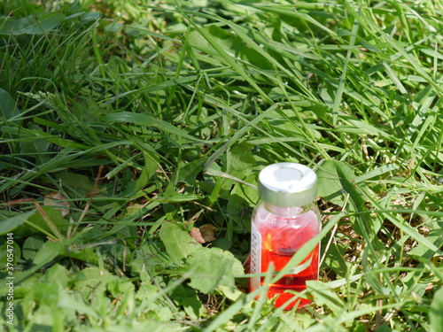 red bottle of medicine on a background of green grass close 