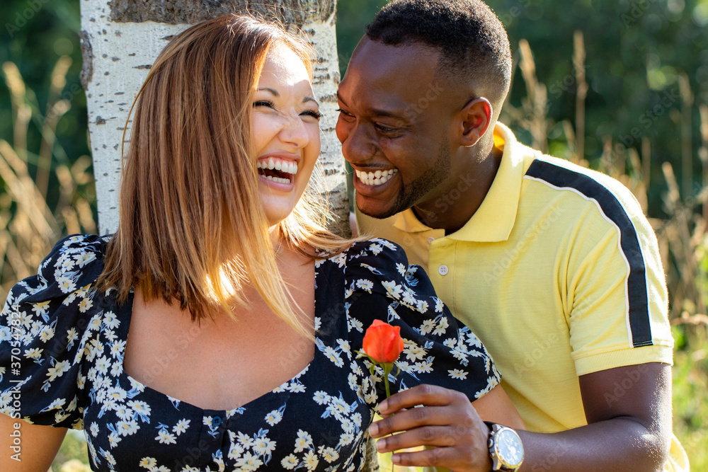 Handsome black guy giving white girlfriend a flower outdoors.