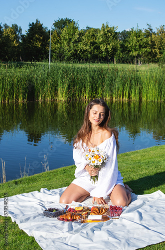 Young smiling woman relaxing outdoors and having a picnic, she is sitting on blanket on the grass.