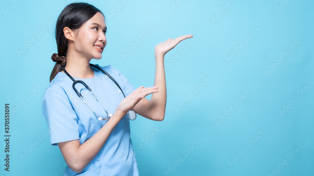 Portrait of young Asian beautiful nurse in blue uniform and wearing a surgical mask for protection from covid19 or disease with big smiled inside pointing and present on copy space blue background Portrait of young Asian beautiful nurse in blue uniform and wearing a surgical mask for protection from covid19 or disease with big smiled inside pointing and present on copy space blue background