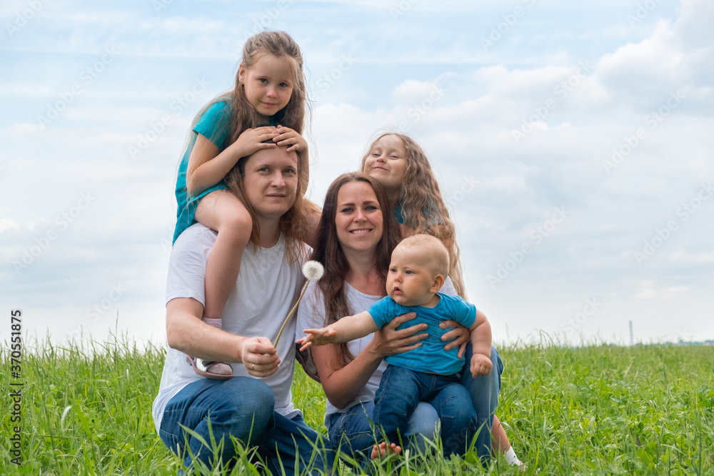 Portrait big family dad, mom and three children on green grass against blue sky. Happy caucasian parents, two daughters and young son. Portrait big family dad, mom and three children on green grass against blue sky. Happy caucasian parents, two daughters and young son.