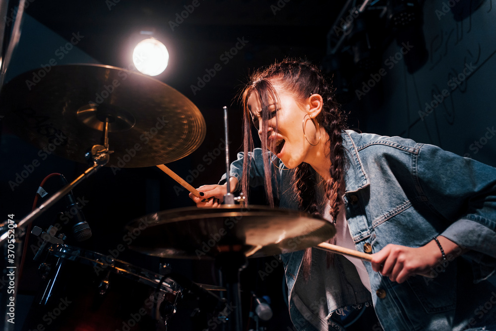 Plays drums. Young beautiful female performer rehearsing in a recording studio Plays drums. Young beautiful female performer rehearsing in a recording studio