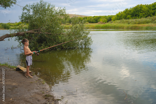 The boy is fishing on a summer river.