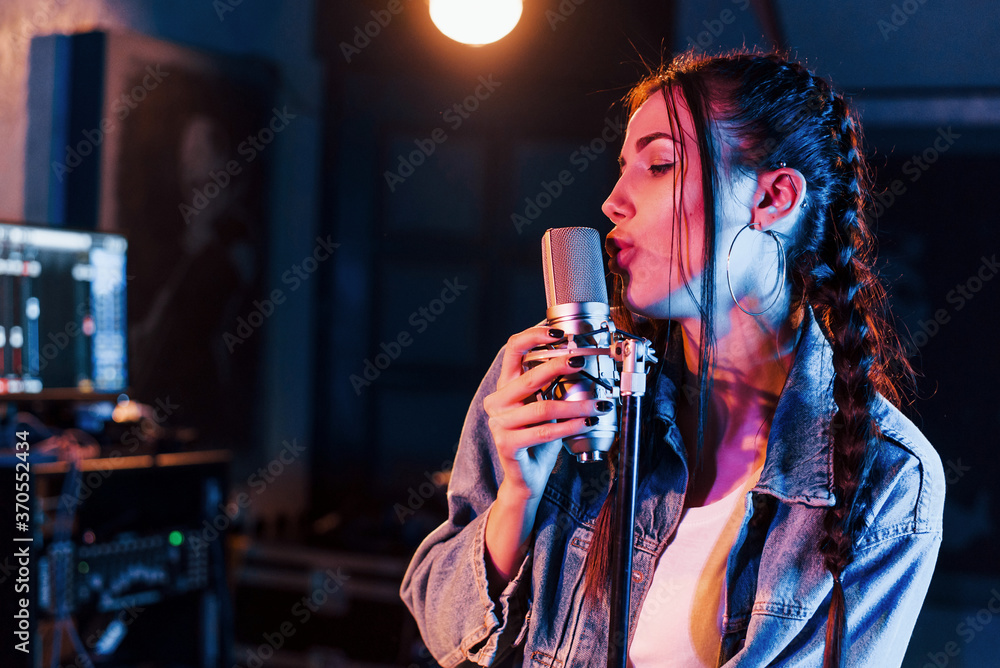 Young beautiful female performer sings and rehearsing in a recording studio