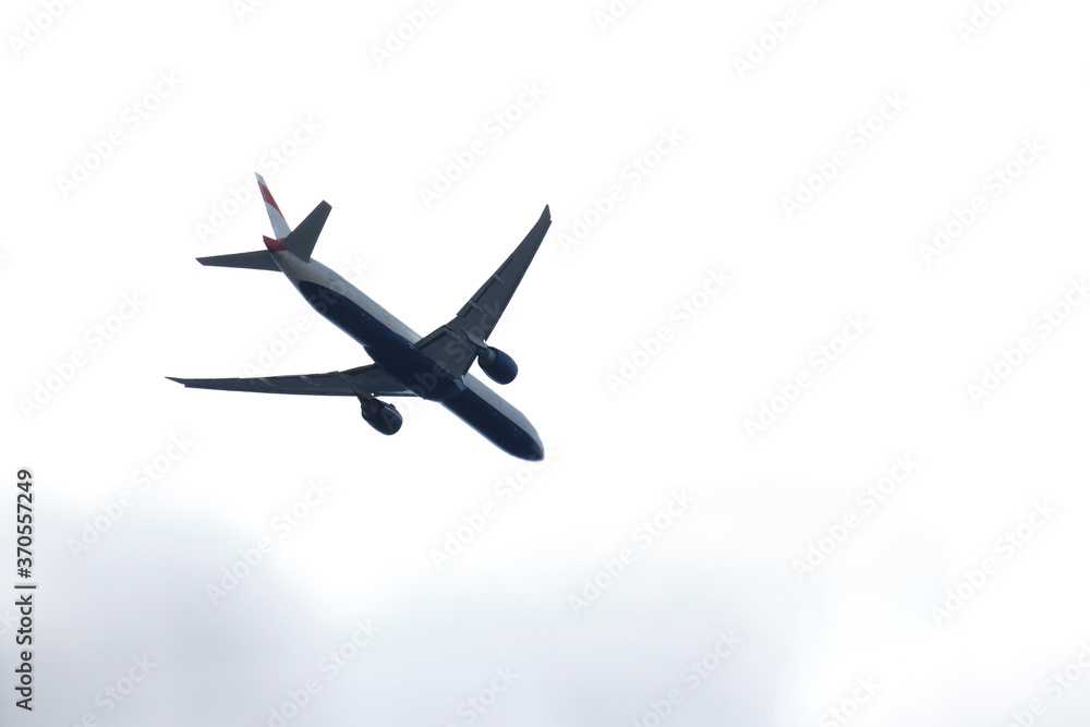 From below of white and blue aircraft flying with cloudy grey sky From below of white and blue aircraft flying with cloudy grey sky