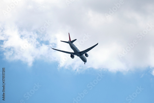 From below of white and blue aircraft flying with blue and cloudy sky