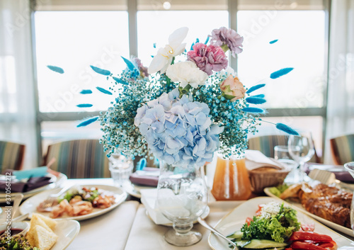 Wedding table setting. Beautiful blue and white bouquet of fresh flowers on the table with food in the restaurant. Wedding decor