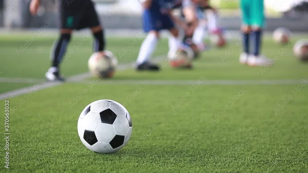 Football on green artificial turf with blurry kid soccer team training. Blurry kid soccer player control ball with coach in soccer academy. Football on green artificial turf with blurry kid soccer team training. Blurry kid soccer player control ball with coach in soccer academy.