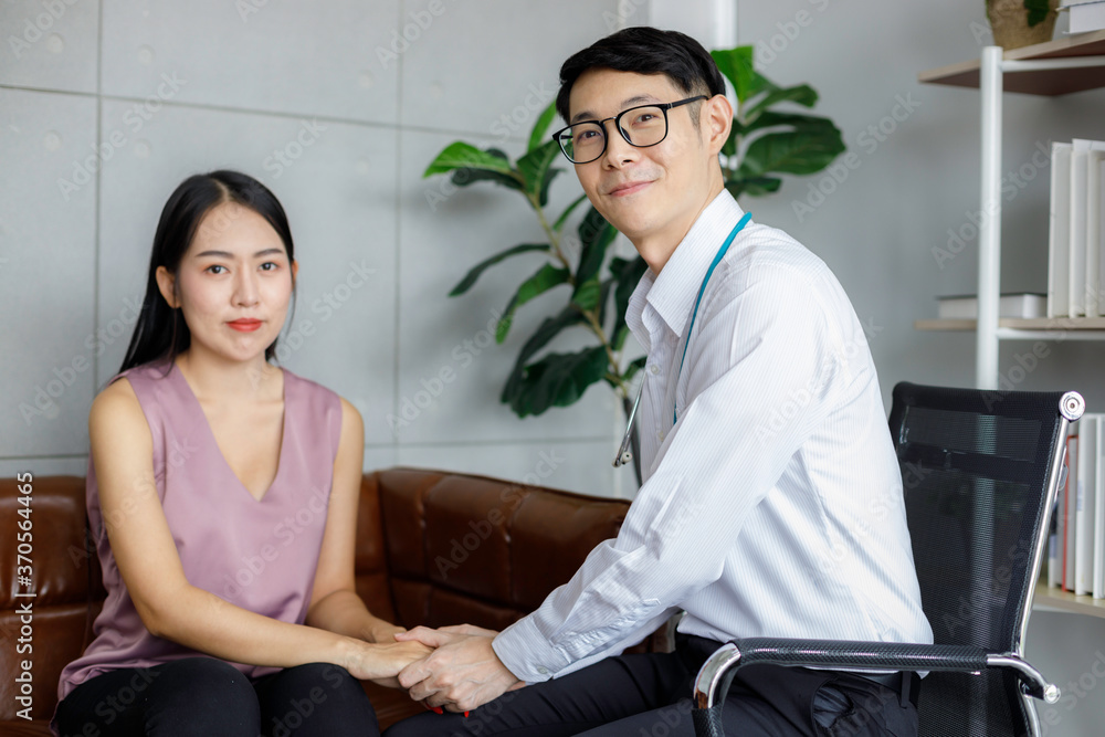 Friendly Asian male doctor's hands holding female patient's hand. They are smile and looking camera. Medical psychology in encouraging and reducing the negative effects of sick people. Friendly Asian male doctor's hands holding female patient's hand. They are smile and looking camera. Medical psychology in encouraging and reducing the negative effects of sick people.