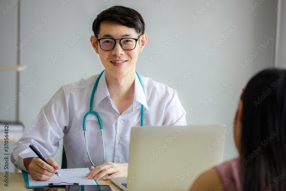 Young Asian male doctor is recording a medical history on the clipboard and explaining something to the female patient. Medical and health care concepts Young Asian male doctor is recording a medical history on the clipboard and explaining something to the female patient. Medical and health care concepts