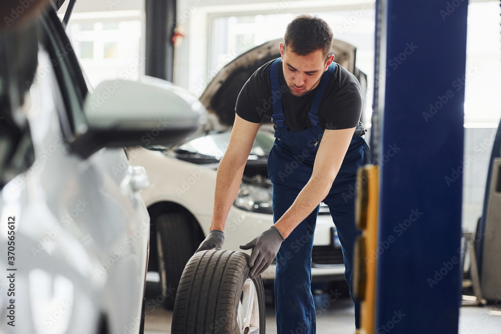 Man in work uniform changing car wheel indoors. Conception of automobile service Man in work uniform changing car wheel indoors. Conception of automobile service