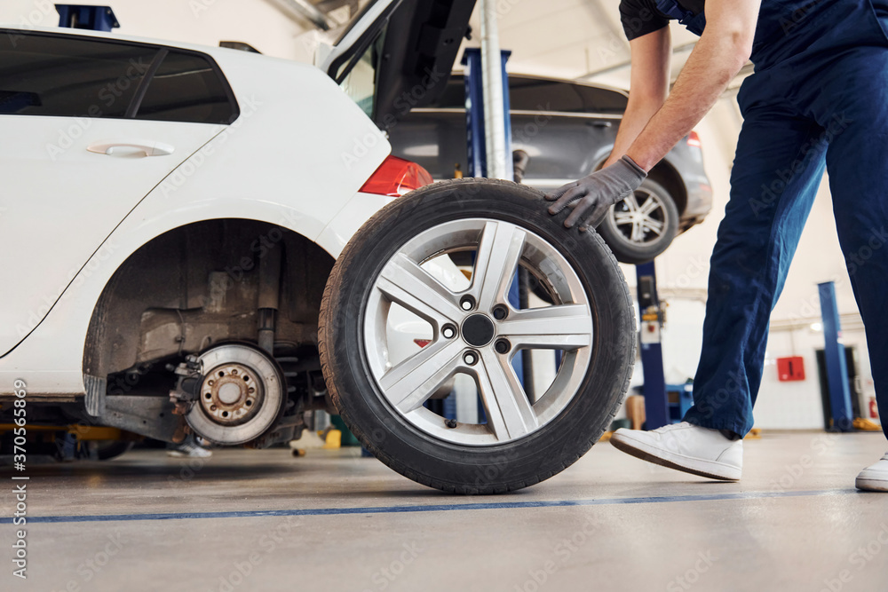 Close up view of man in work uniform with car wheel indoors. Conception of automobile service Close up view of man in work uniform with car wheel indoors. Conception of automobile service
