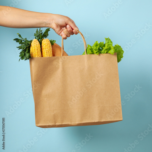 Female hand holds bag with different food on blue background photo