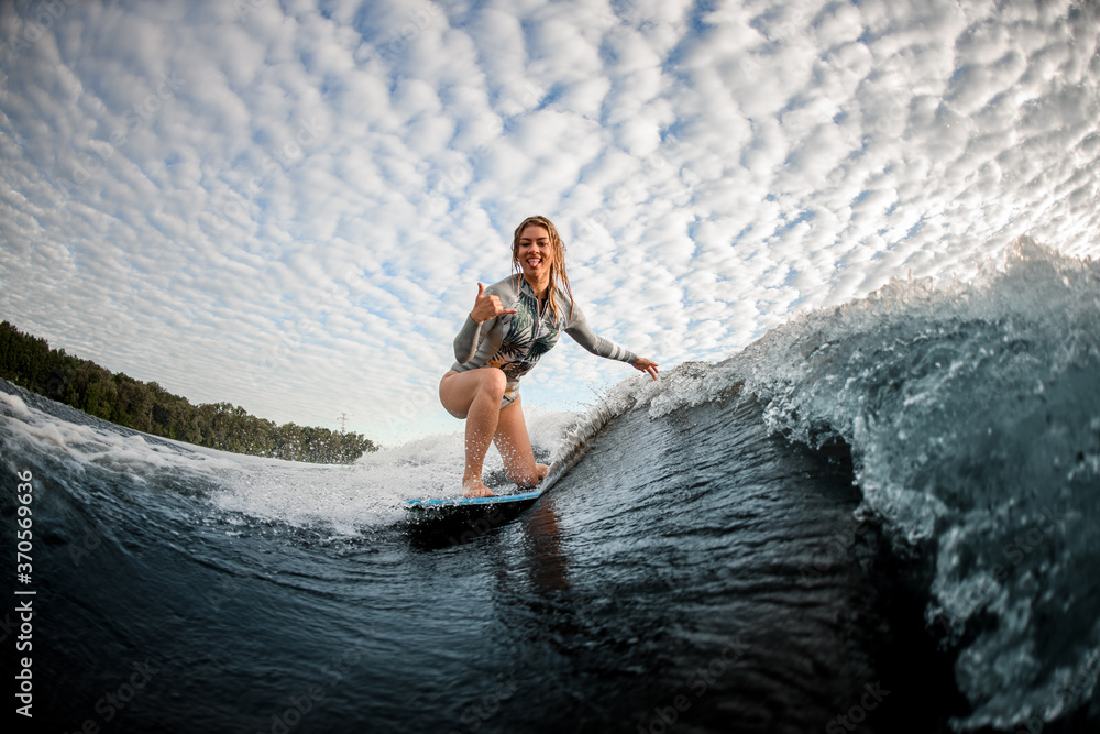 cheerful blonde woman riding down the wave on wakesurf board