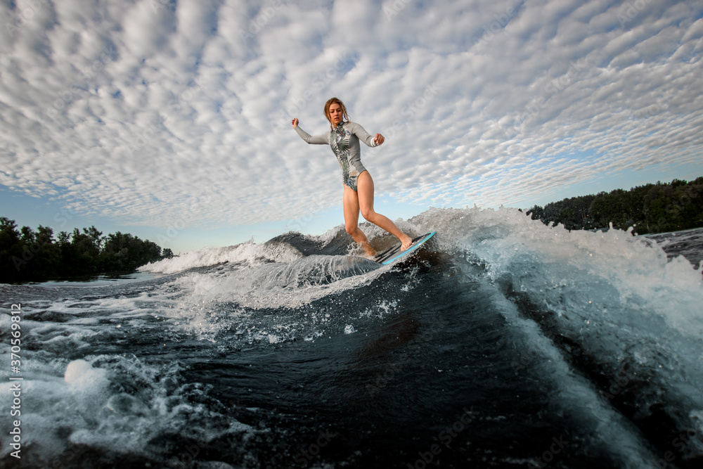 view of young woman who standing on wakesurf board and riding the wave