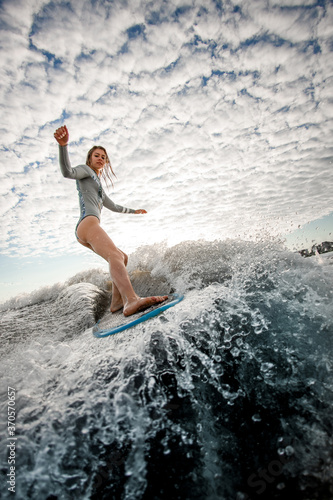 woman with wet hair rides down the wave on surfboard against cloudy sky background