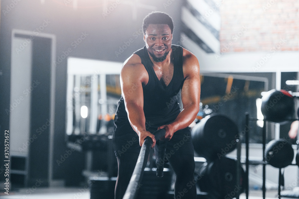 Strong african american man in sportive clothes have workout day in the gym. Doing crossfit by using ropes Strong african american man in sportive clothes have workout day in the gym. Doing crossfit by using ropes