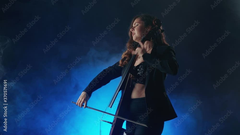 Young beautiful woman playing a melody on cello. Smoky dark studio Young beautiful woman playing a melody on cello. Smoky dark studio